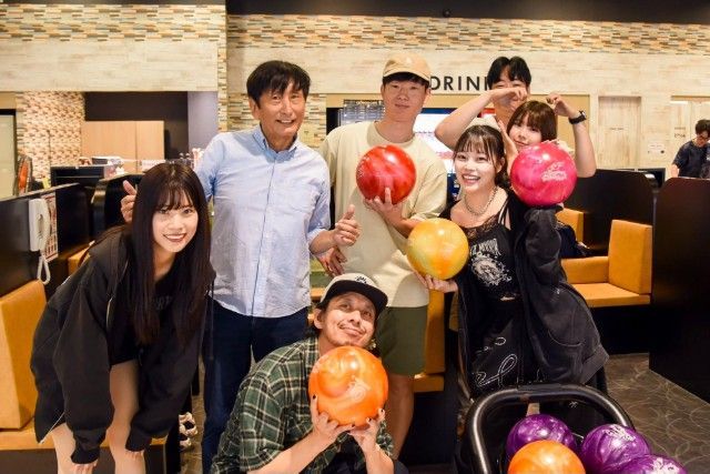 Group of people at a bowling alley, holding bowling balls, smiling for the camera.