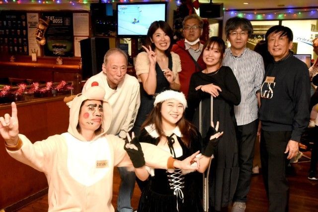 Group of nine people posing in a bar, some wearing costumes, smiling. Christmas decorations visible.