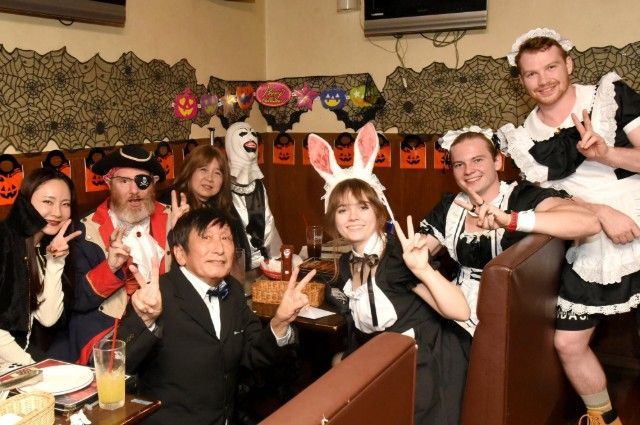 People in costumes at a Halloween-themed restaurant. They are making peace signs, smiling, and posing for a photo.