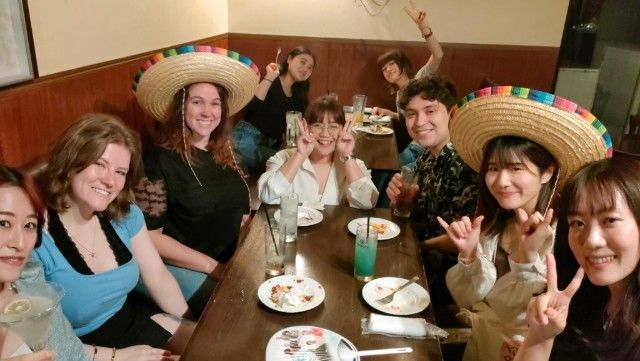 Group of people at a restaurant table, some wearing sombreros and making hand gestures, smiling, and having drinks.