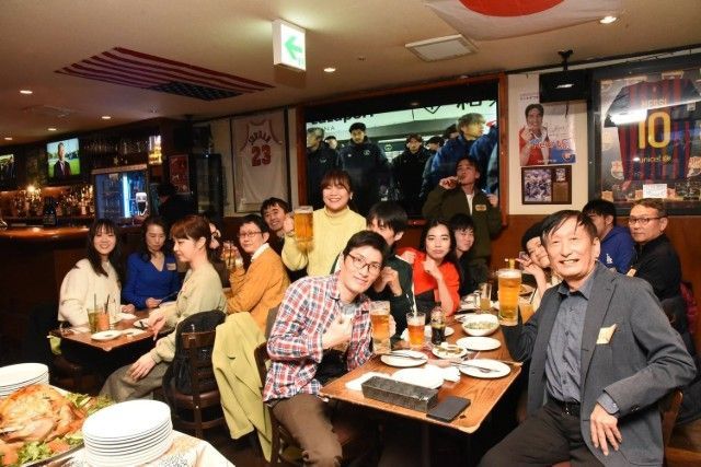 People at a lively bar, drinking beer, watching a screen, and enjoying each other's company.