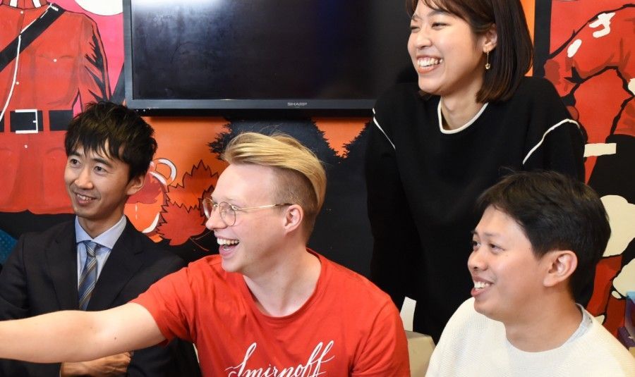 Four people smiling and talking in a casual indoor setting, with red and black wall art behind them