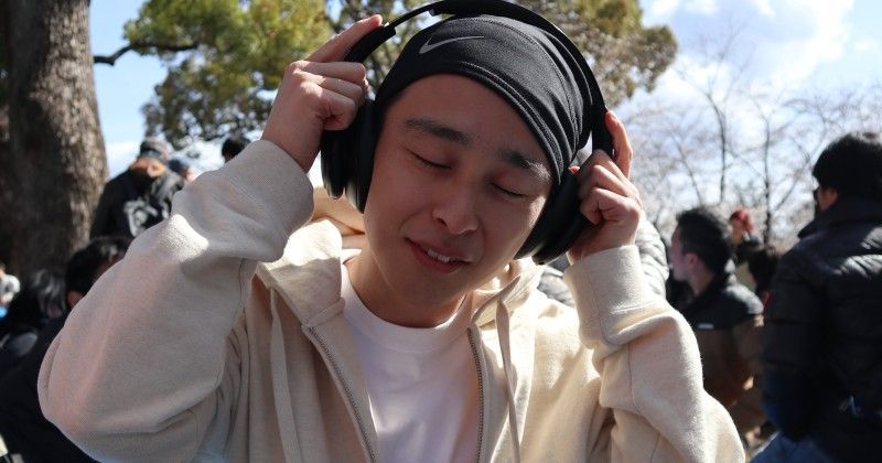 Person wearing headphones outdoors, eyes closed, adjusting them in bright sunlight