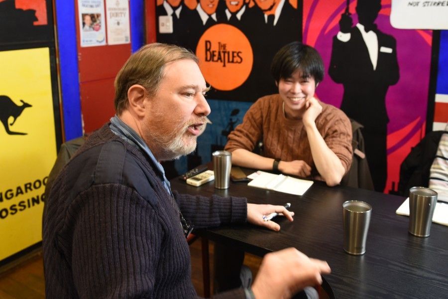 An English teacher and a student are sitting at a table in front of a Beatles poster.