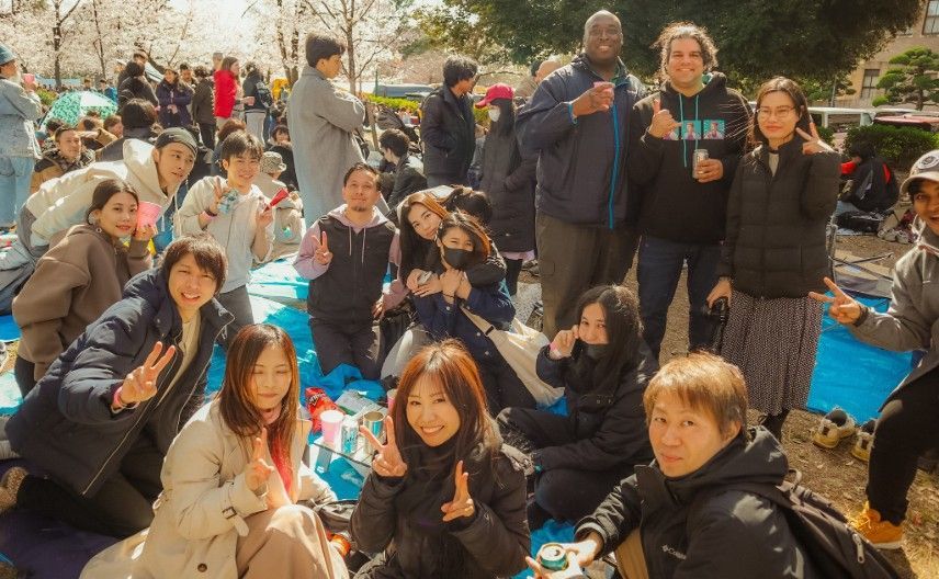 Group of people smiling enjoying a Hanami Party picnic in a park in Nagoya.