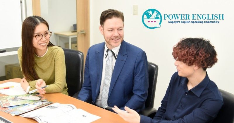 Three people are sitting at a wooden table in an office, discussing documents and having a conversation.