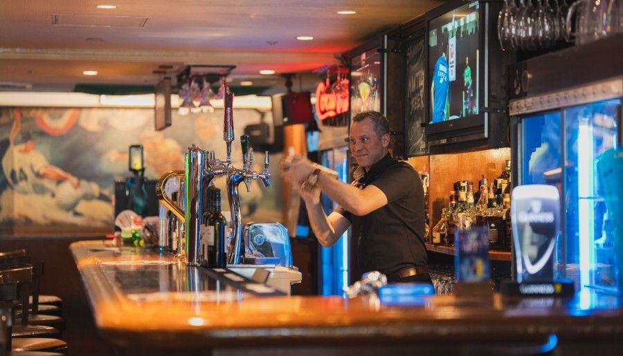 A person works behind a bar, preparing a drink at the tap in a dimly lit, cozy pub setting.
