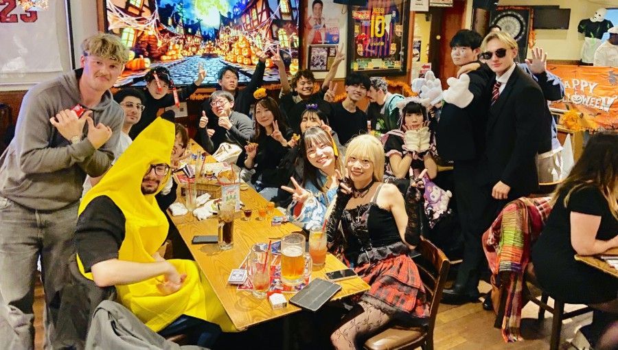 Group of costumed people at a pub, celebrating. Includes a banana, and a person in a suit, all smiling.
