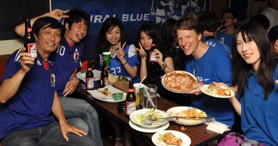 A group of people are sitting at a table eating pizza and drinking beer.