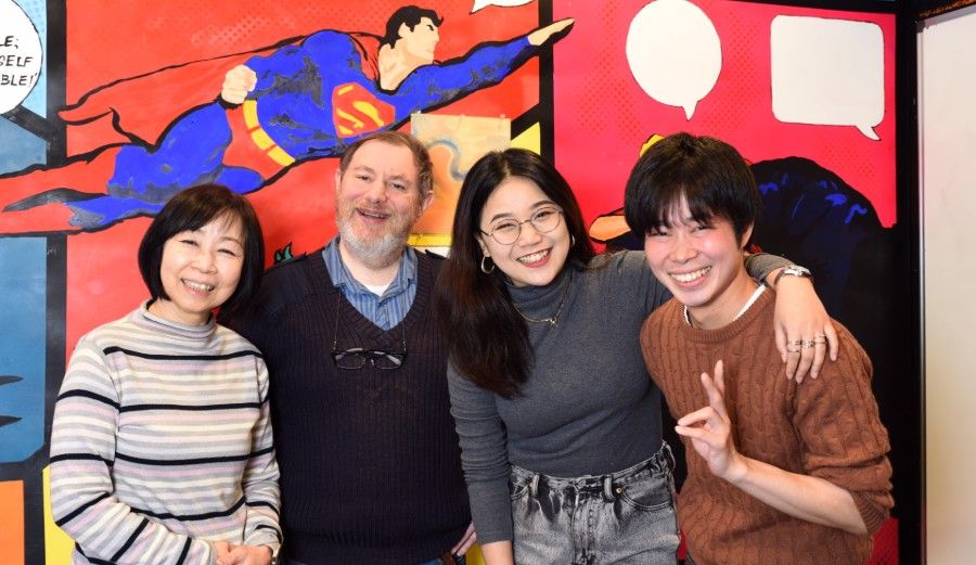 Four people pose for a photo in front of a Superman mural.