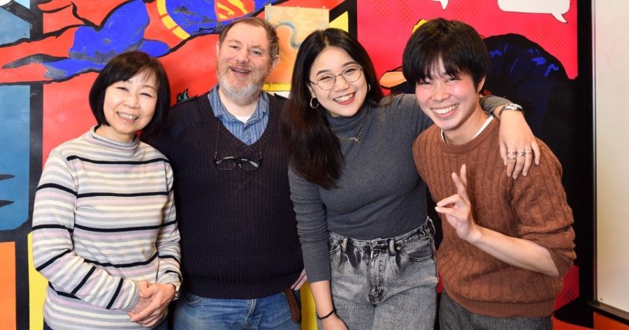 Four people smiling, posing together in front of a colorful wall mural.