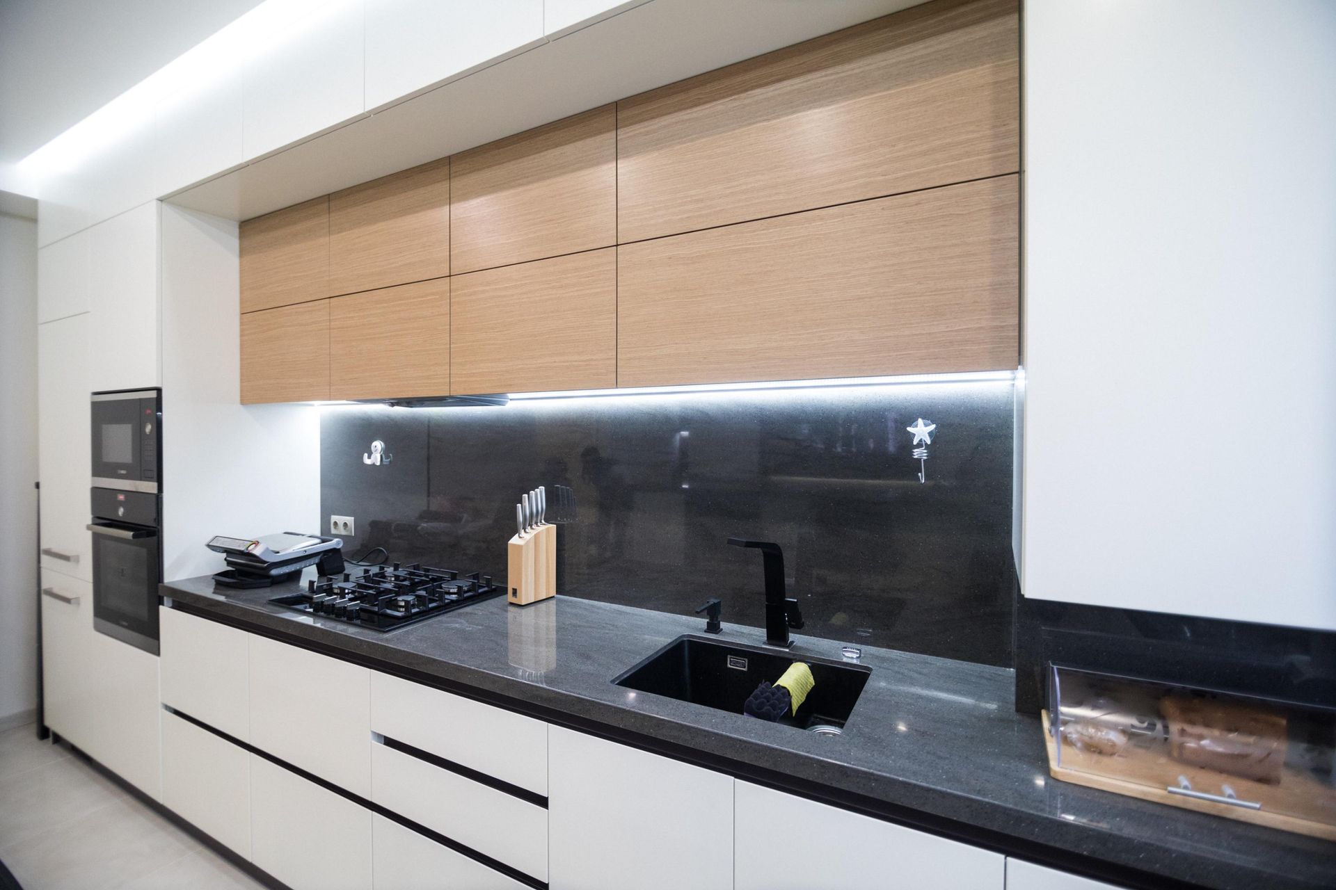 Modern kitchen with white and wood cabinetry, black countertops, and backsplash.