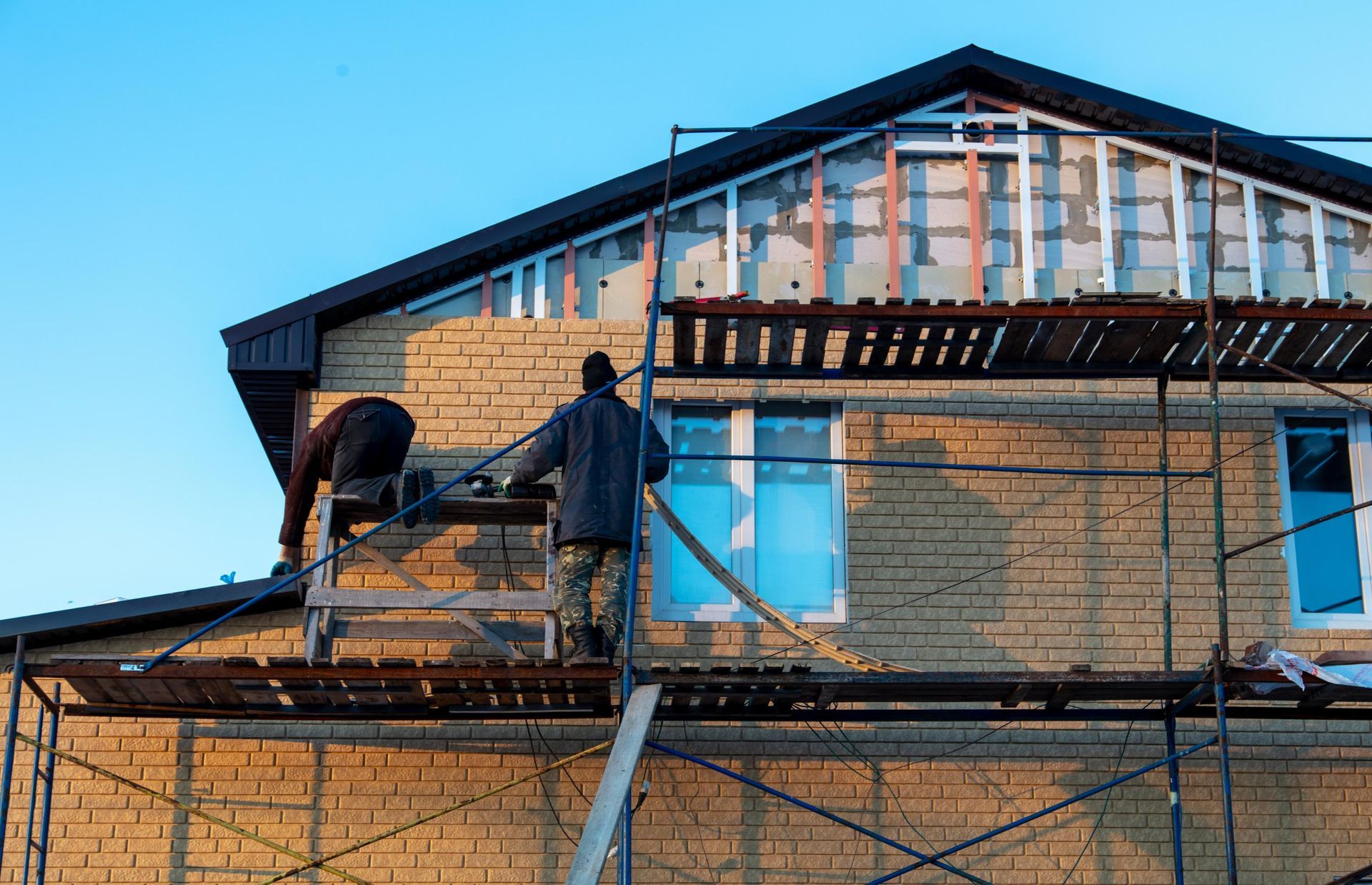 Construction workers on scaffolding, installing siding on a two-story brick building.
