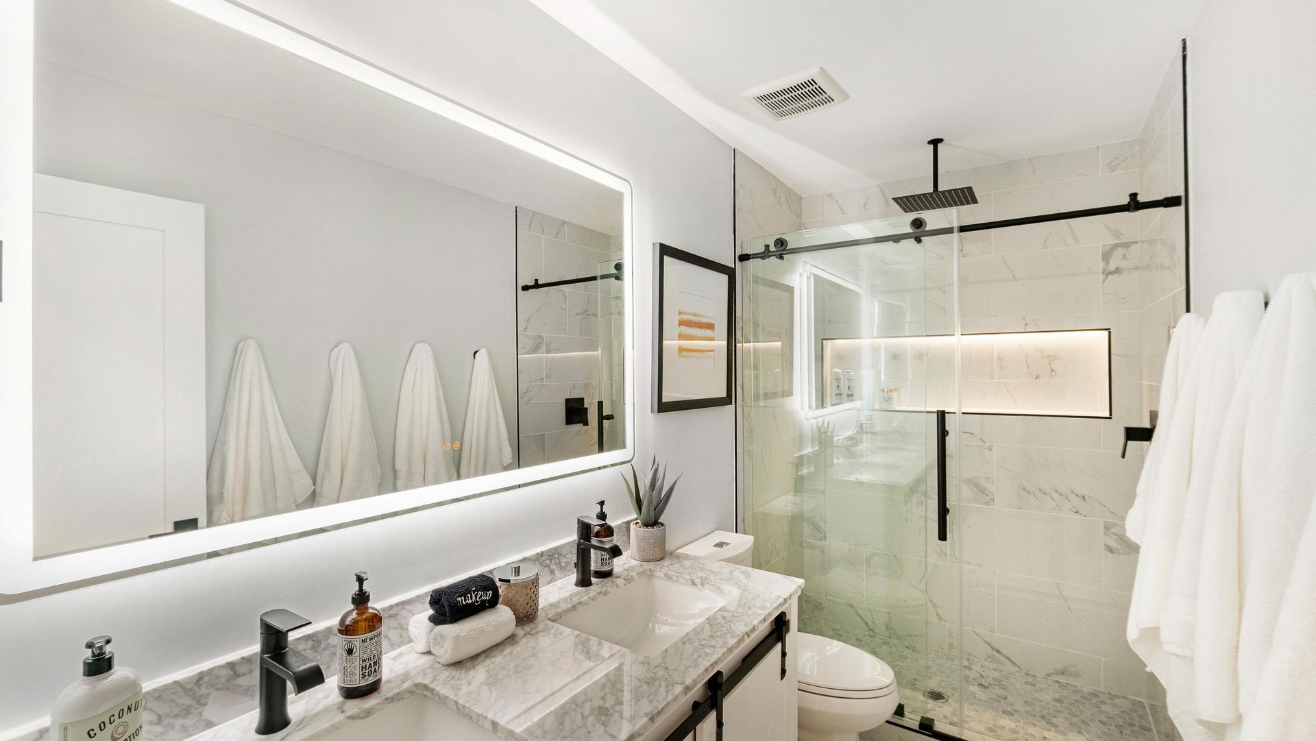 Modern bathroom with marble countertop, large mirror, and glass shower door. White towels.