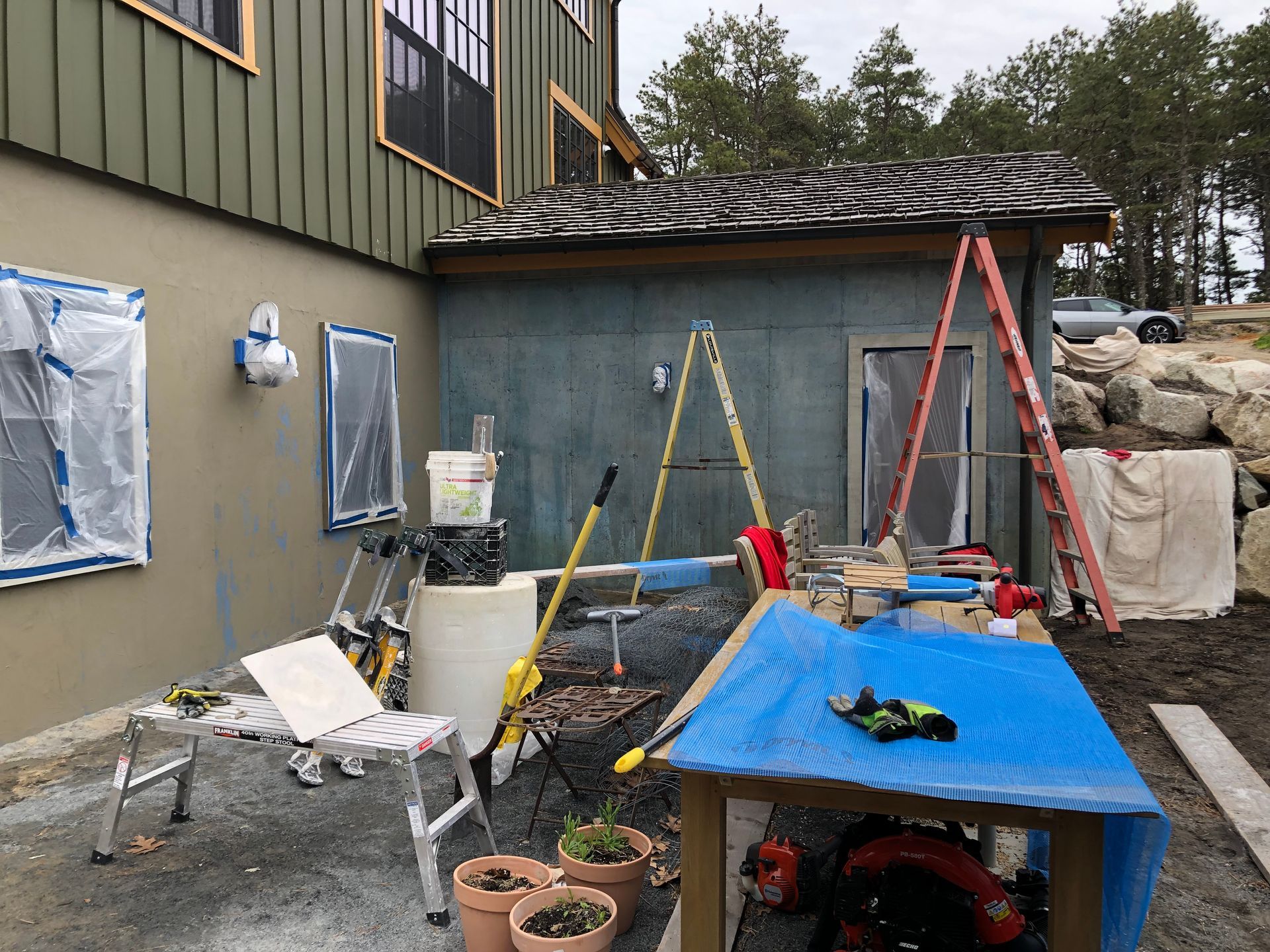 Construction site: tools, ladders, covered windows, stucco wall, and small building under renovation.