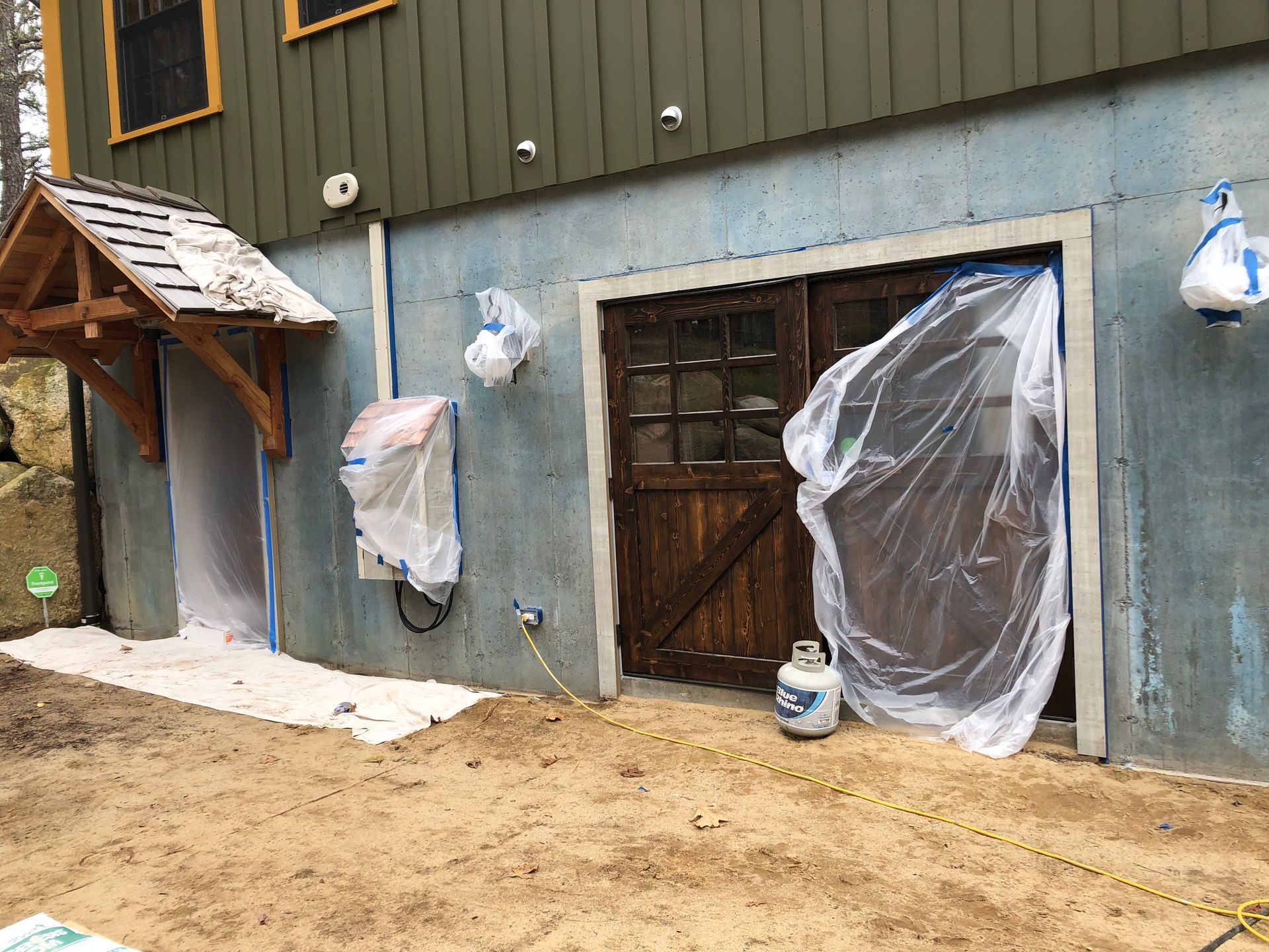 Exterior of a building with blue concrete walls. Doors and a small entryway are covered with plastic sheeting.