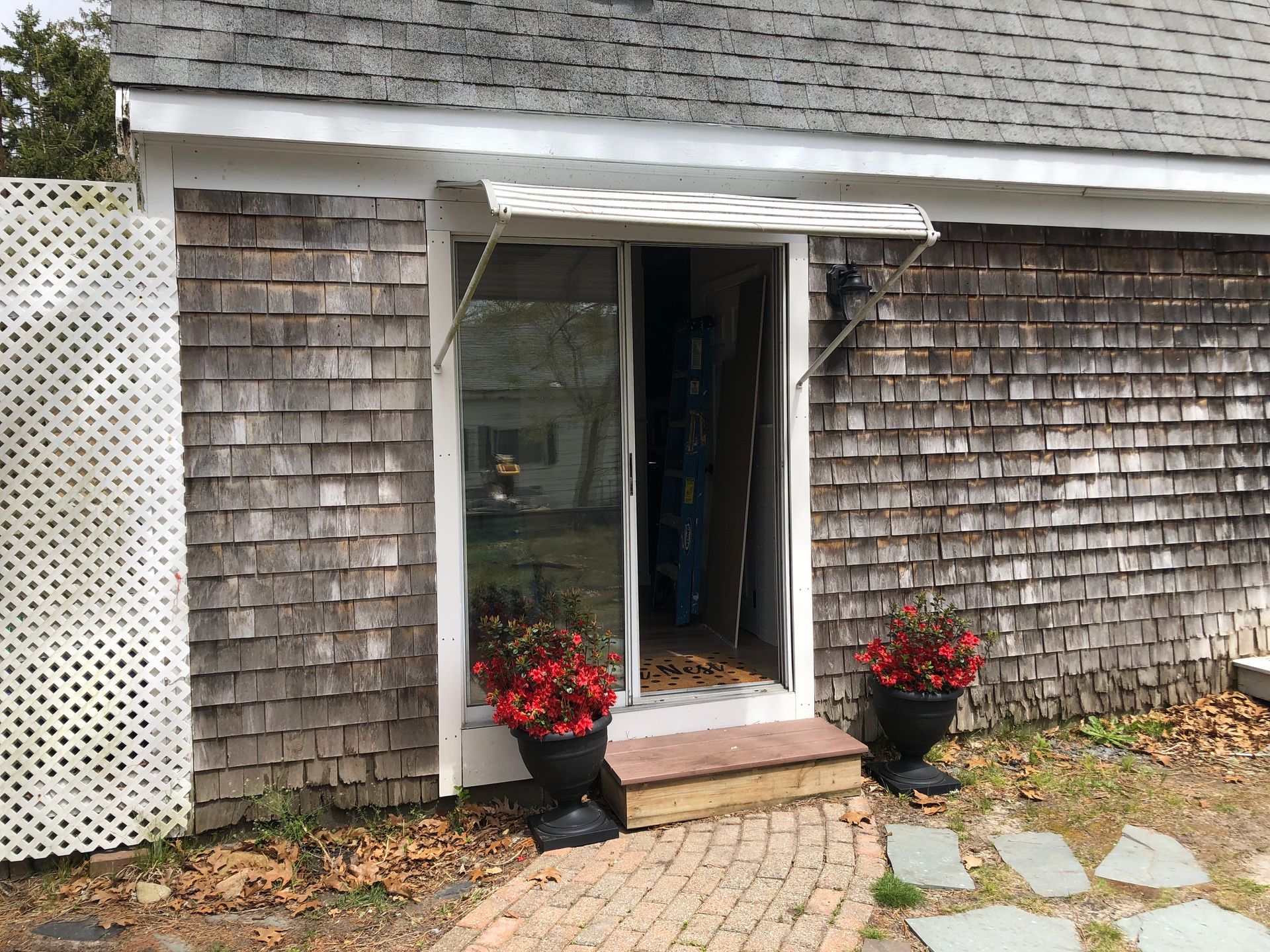 Sliding glass door entrance with awning, flanked by weathered wood siding and flower pots.