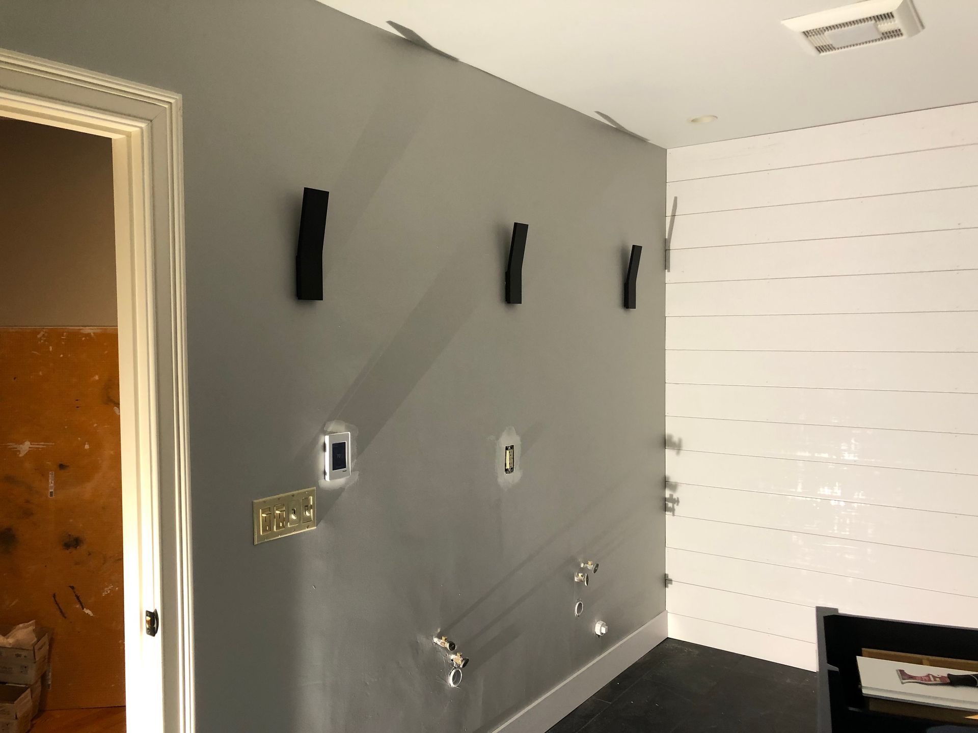 Gray and white walls in a room, partially under construction, with exposed electrical wiring and black objects on the wall.