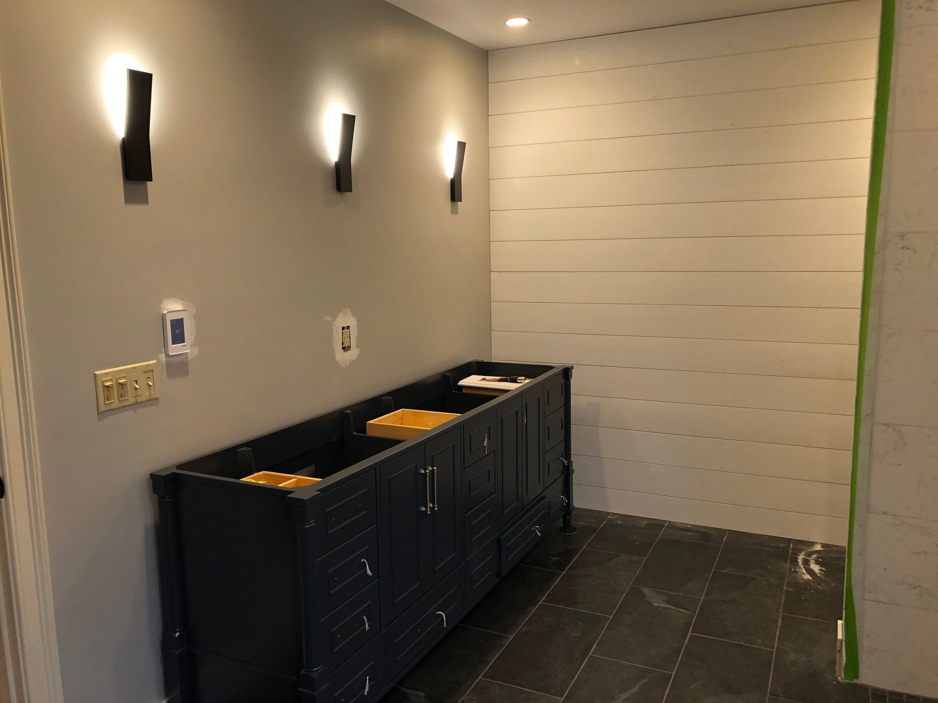 Bathroom with dark blue vanity, gray walls, three sconces, and planked white wall.