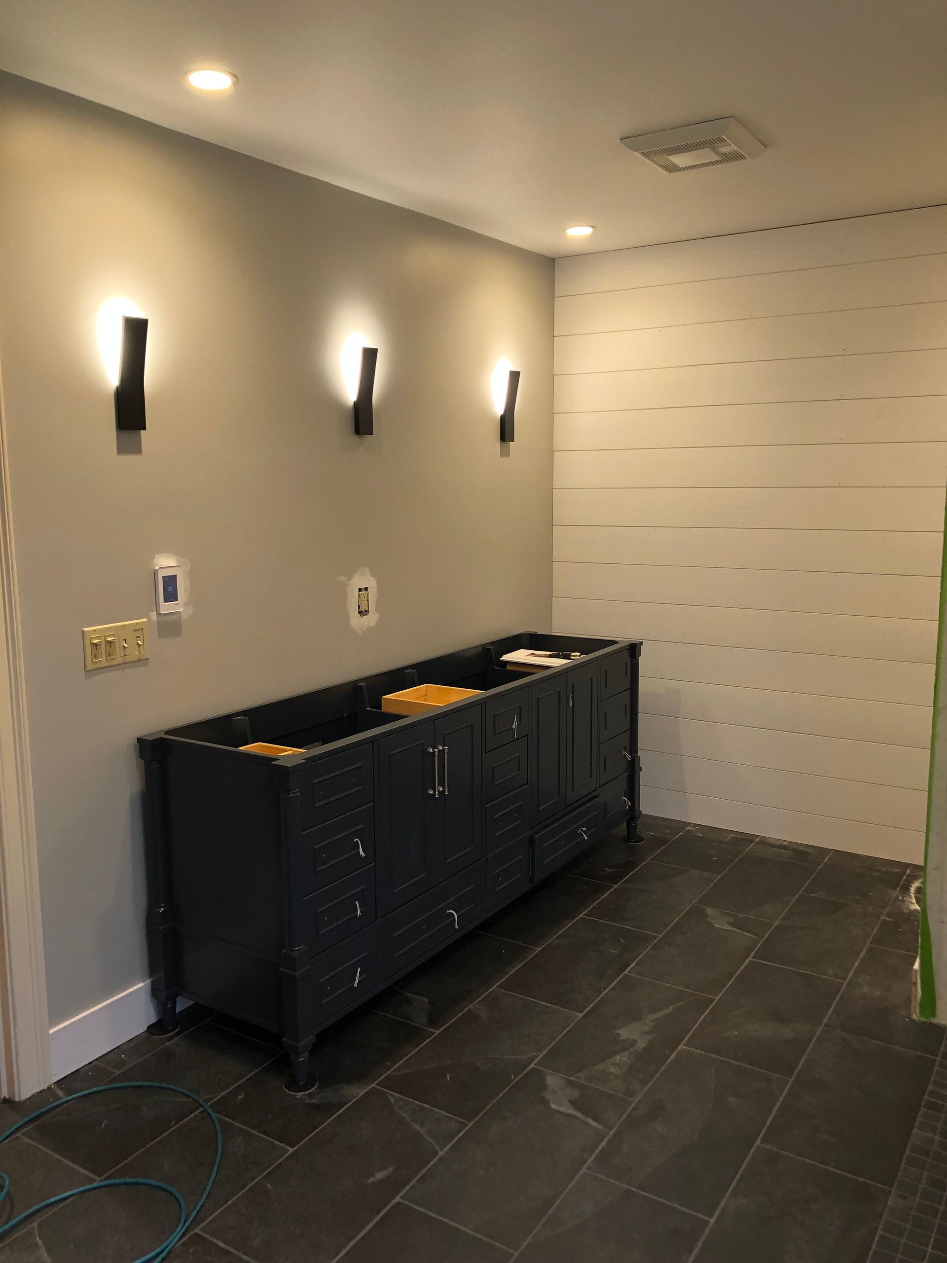 Bathroom with dark blue vanity, gray walls, three sconces, and slate tile floor.