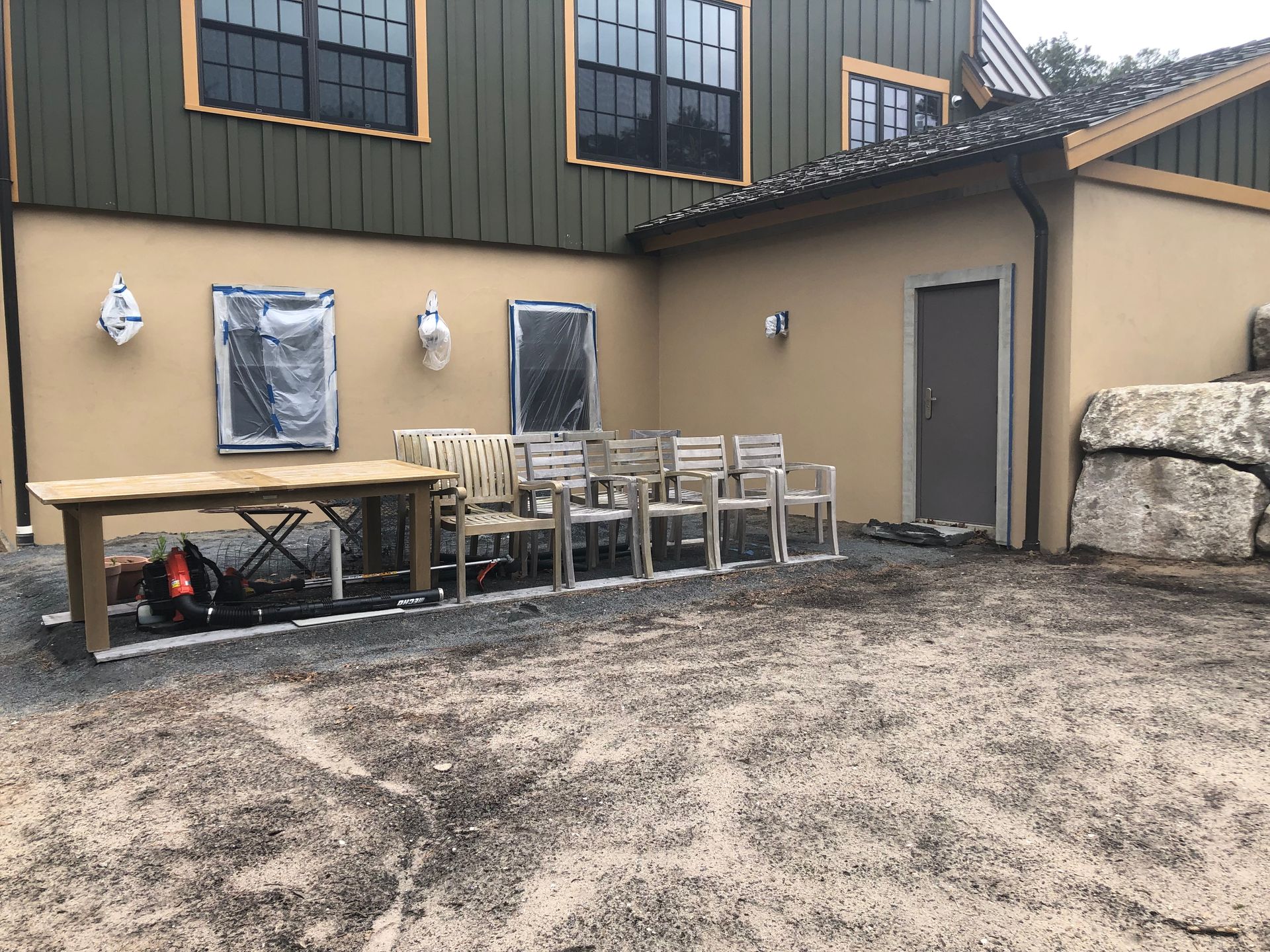 Exterior view of building with chairs, table, and door on gravel ground.