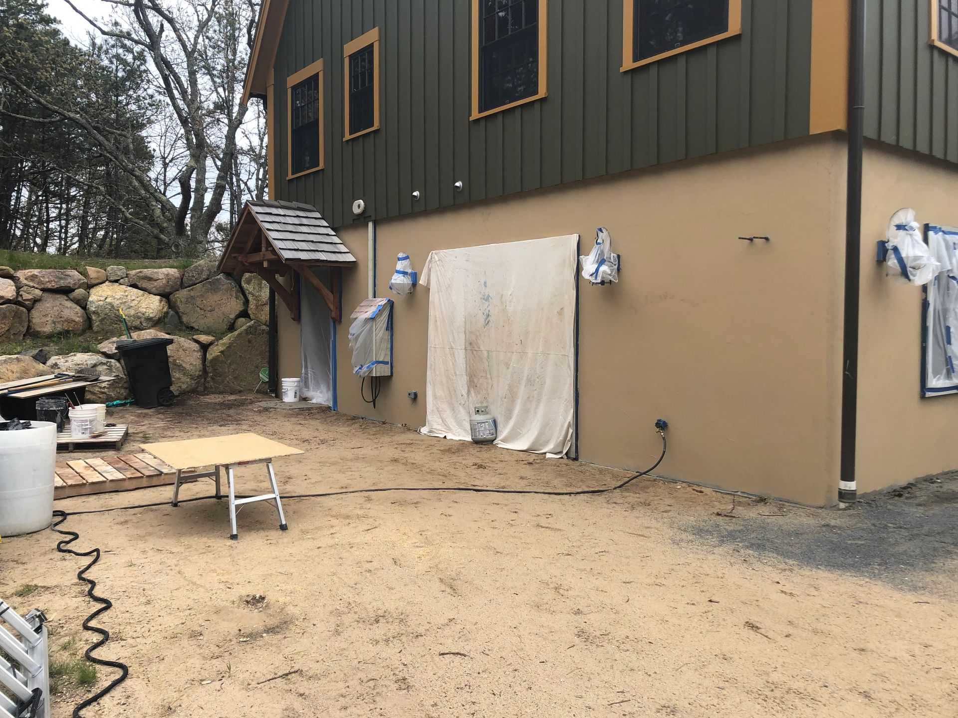 Exterior of a two-story building being renovated; beige stucco wall, green siding.