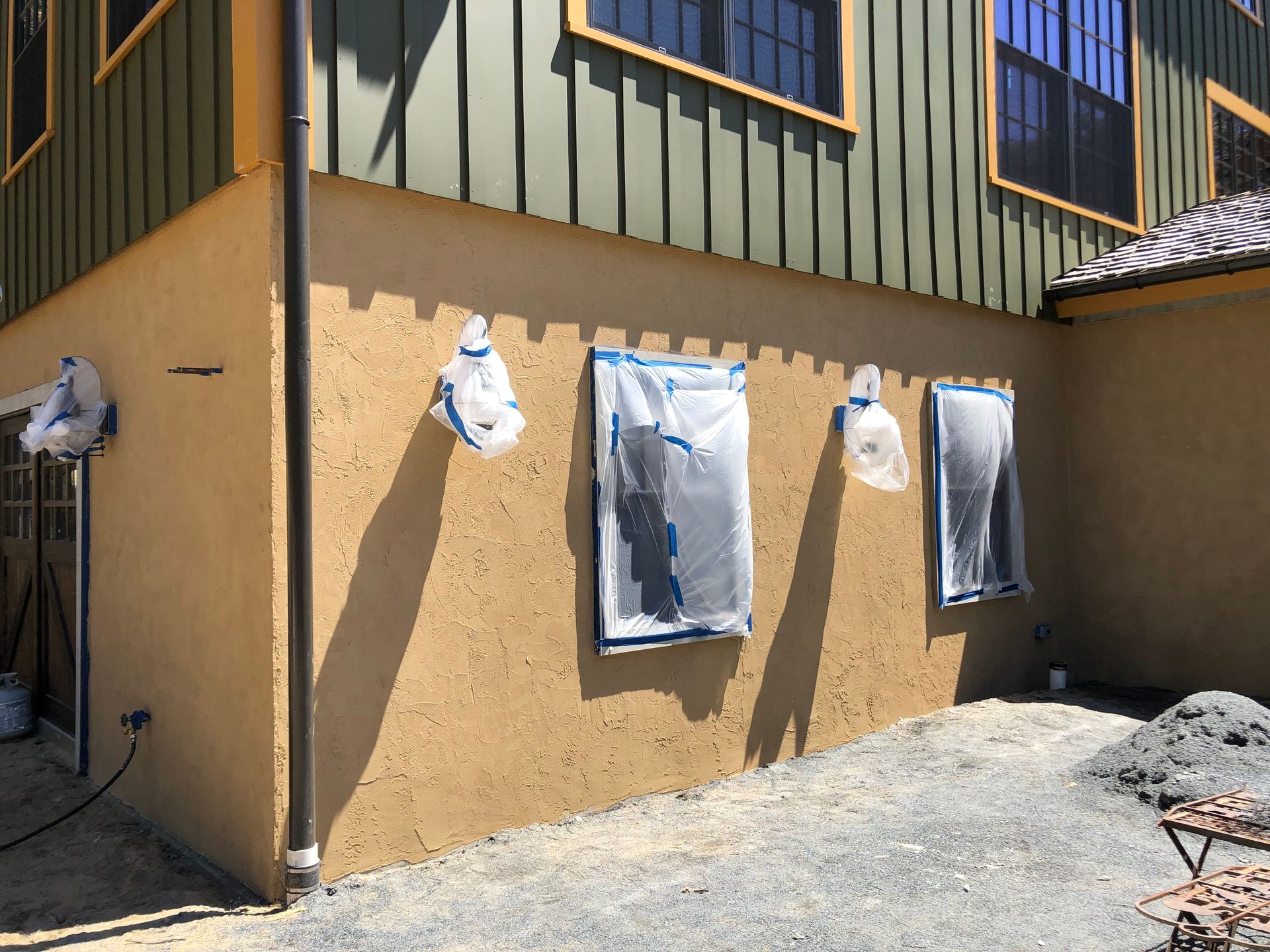 Exterior wall with stucco finish, windows covered, under green siding.