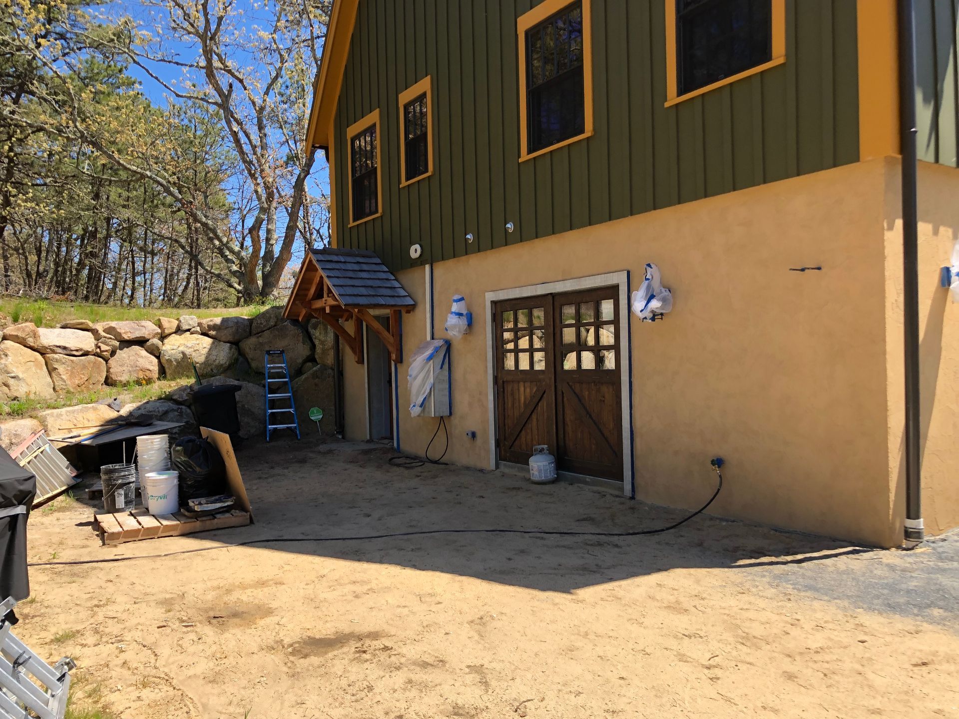 Building exterior with olive green siding, yellow trim, and tan stucco, with wooden double doors and a porch.