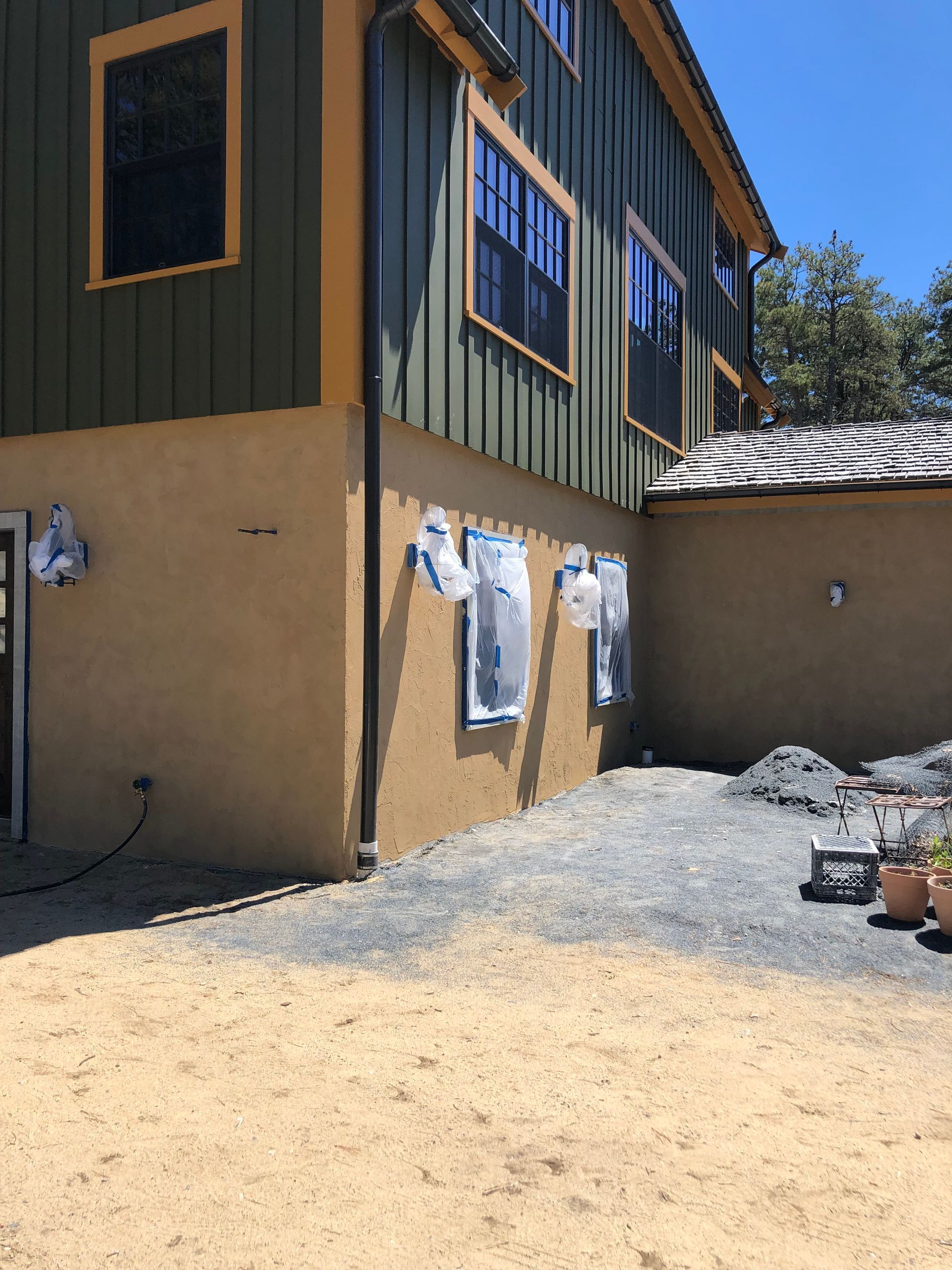Exterior view of a two-story building with green siding and stucco base under construction. Windows are taped off.