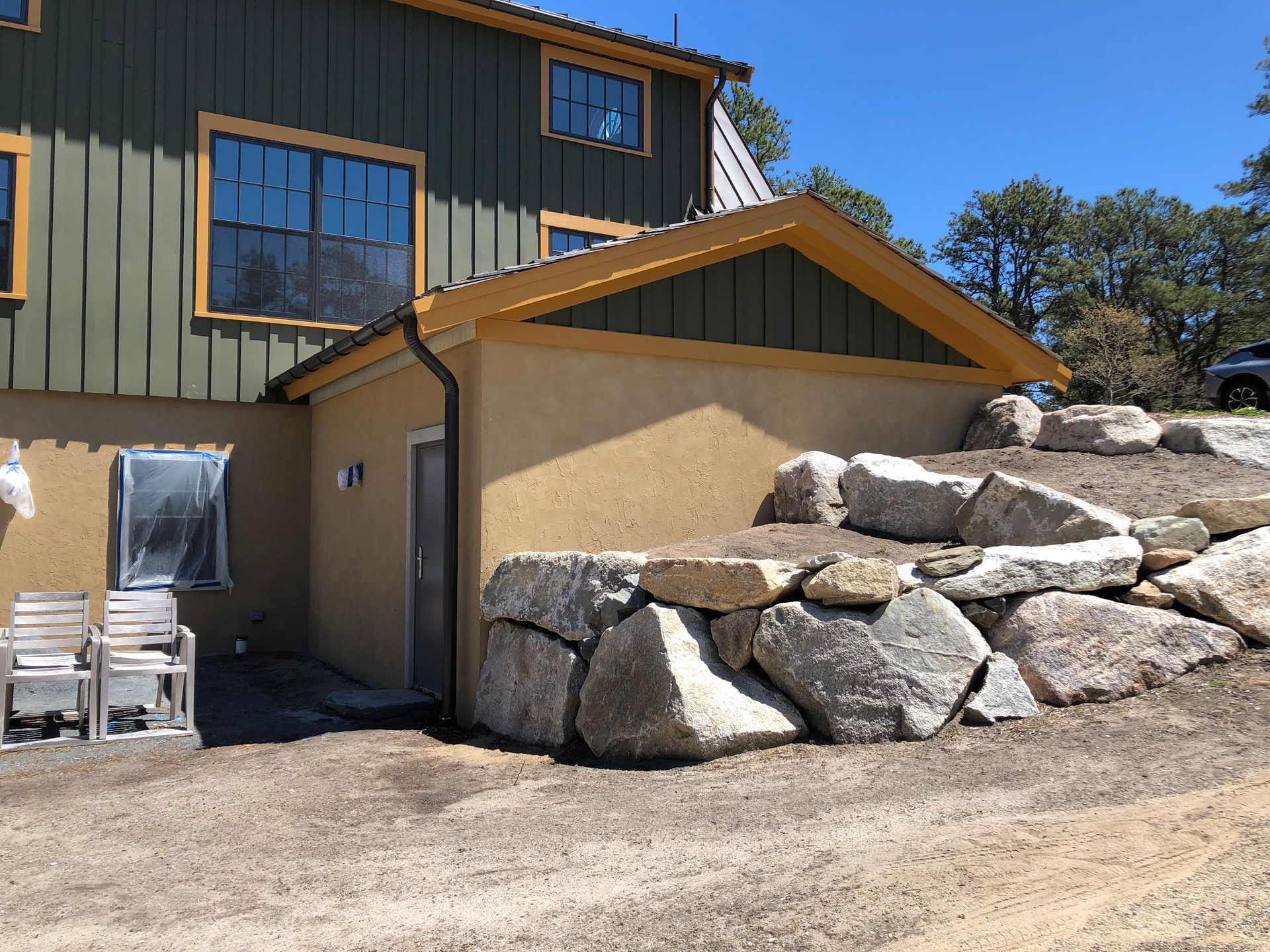 Tan stucco building with a rock retaining wall and green siding under a blue sky.