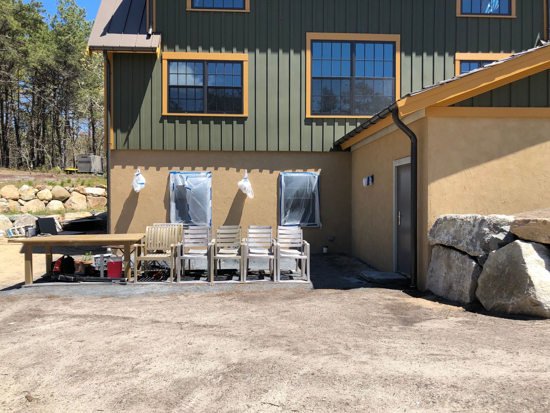 Building exterior with green siding, stucco, windows, and chairs on gravel patio.