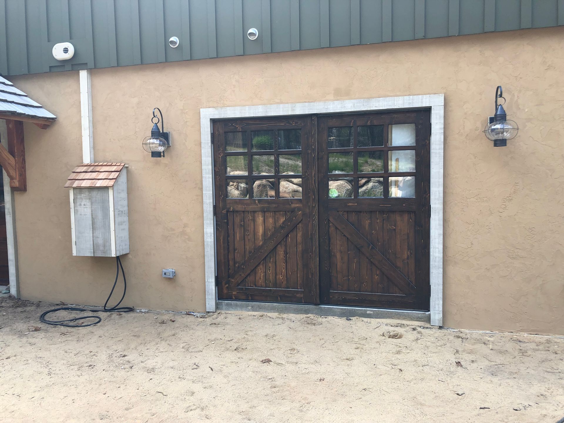 Rustic wooden double doors with glass panes set in a tan stucco wall, flanked by sconces.