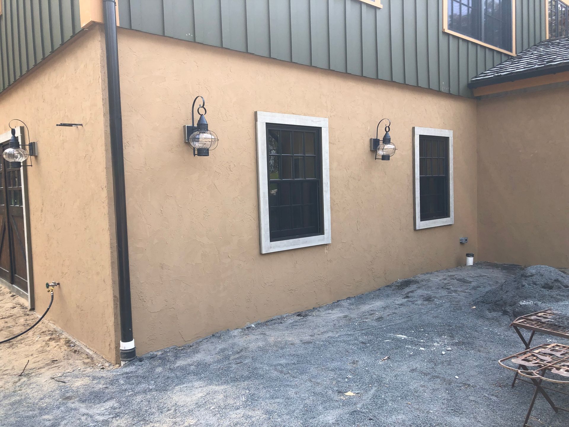 Tan stucco building with two windows and ornate outdoor lights, surrounded by gravel.