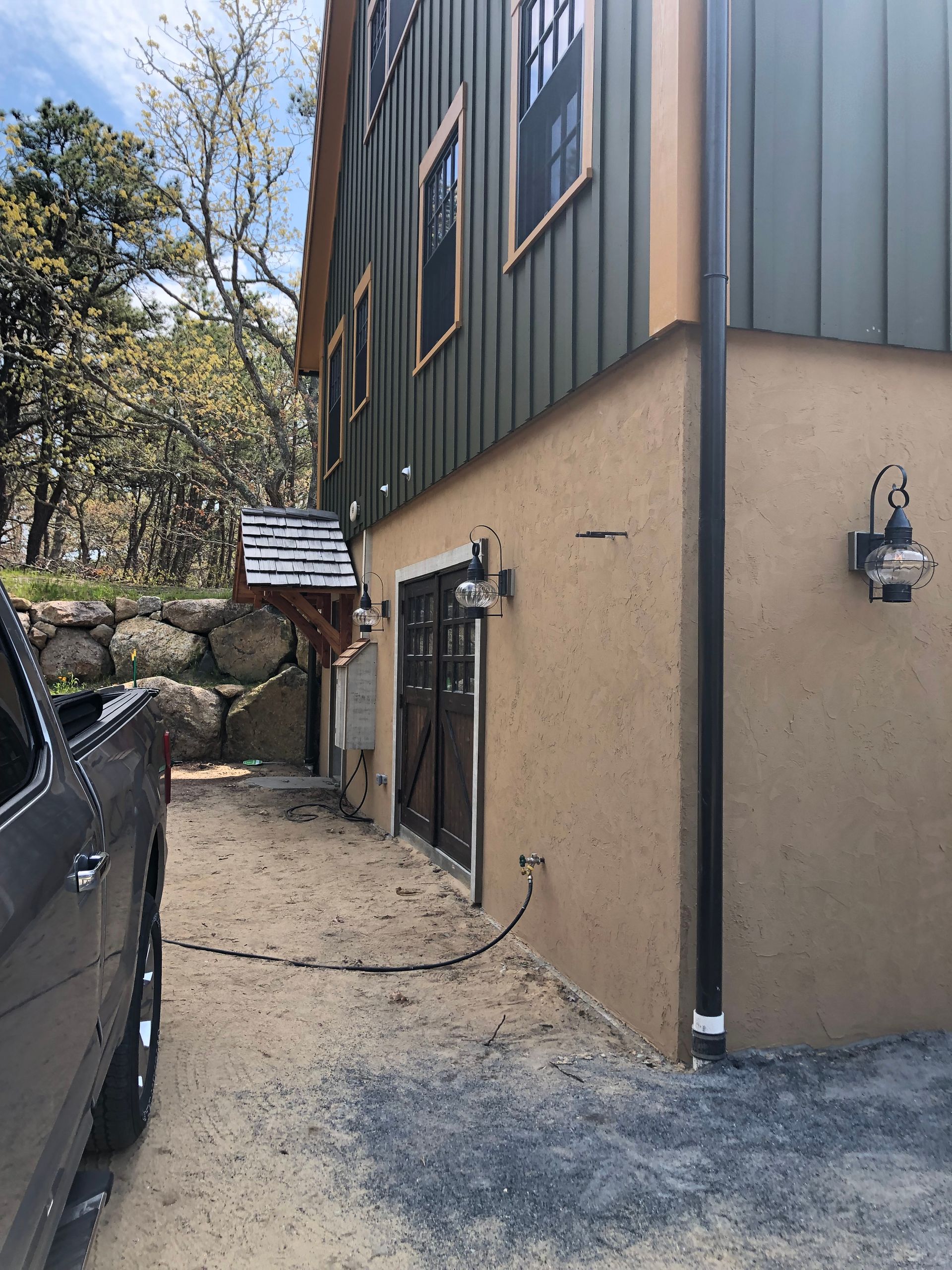Side view of a building with green siding and tan stucco. A car is parked on the left.