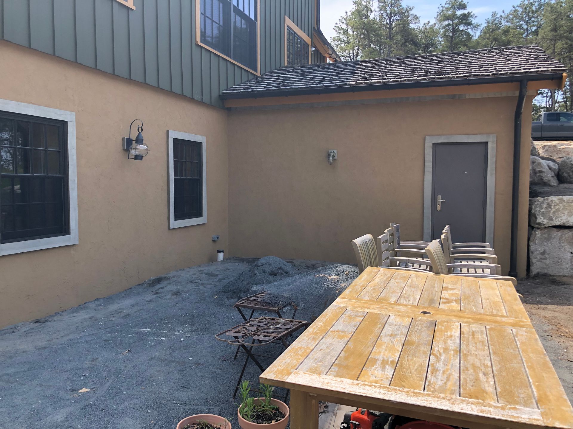 Outdoor patio with gravel, wood table, chairs, and tan building.
