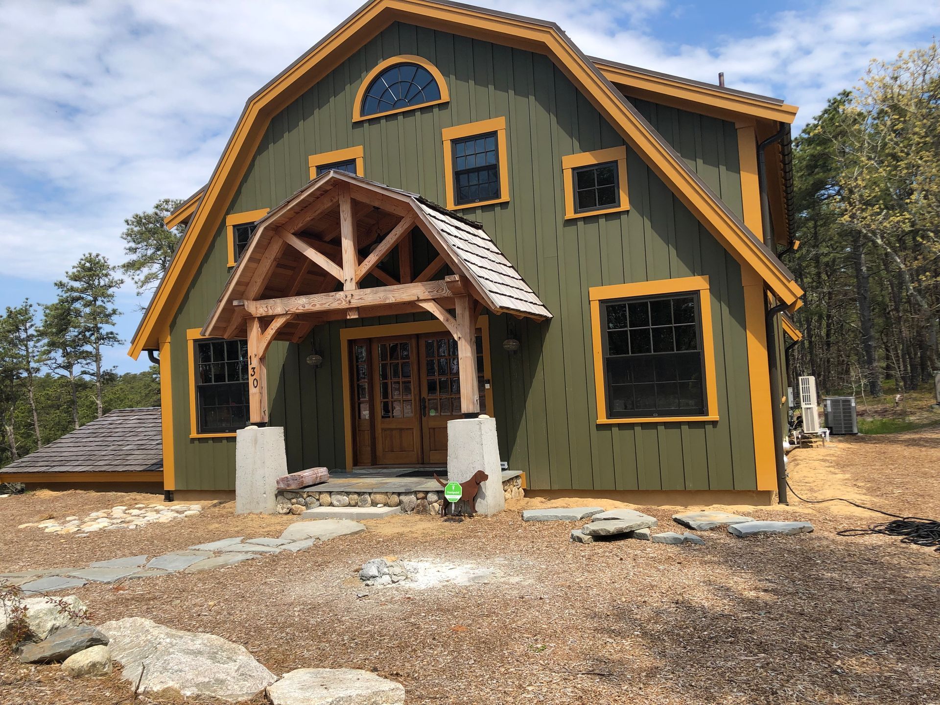 Green and gold barn-style house with wooden porch, stone steps, and arched window.