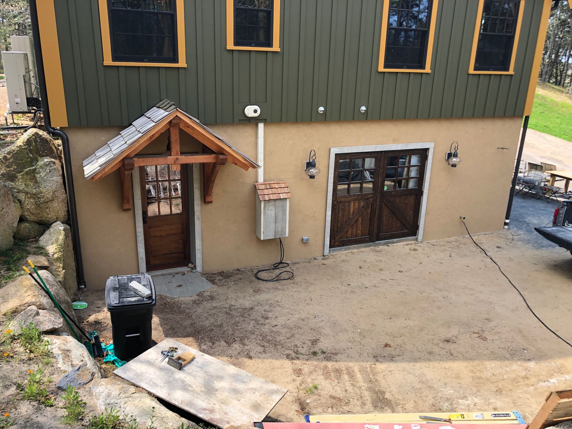 Exterior of a two-story building with a garage, a door with a small overhang, and dirt ground.