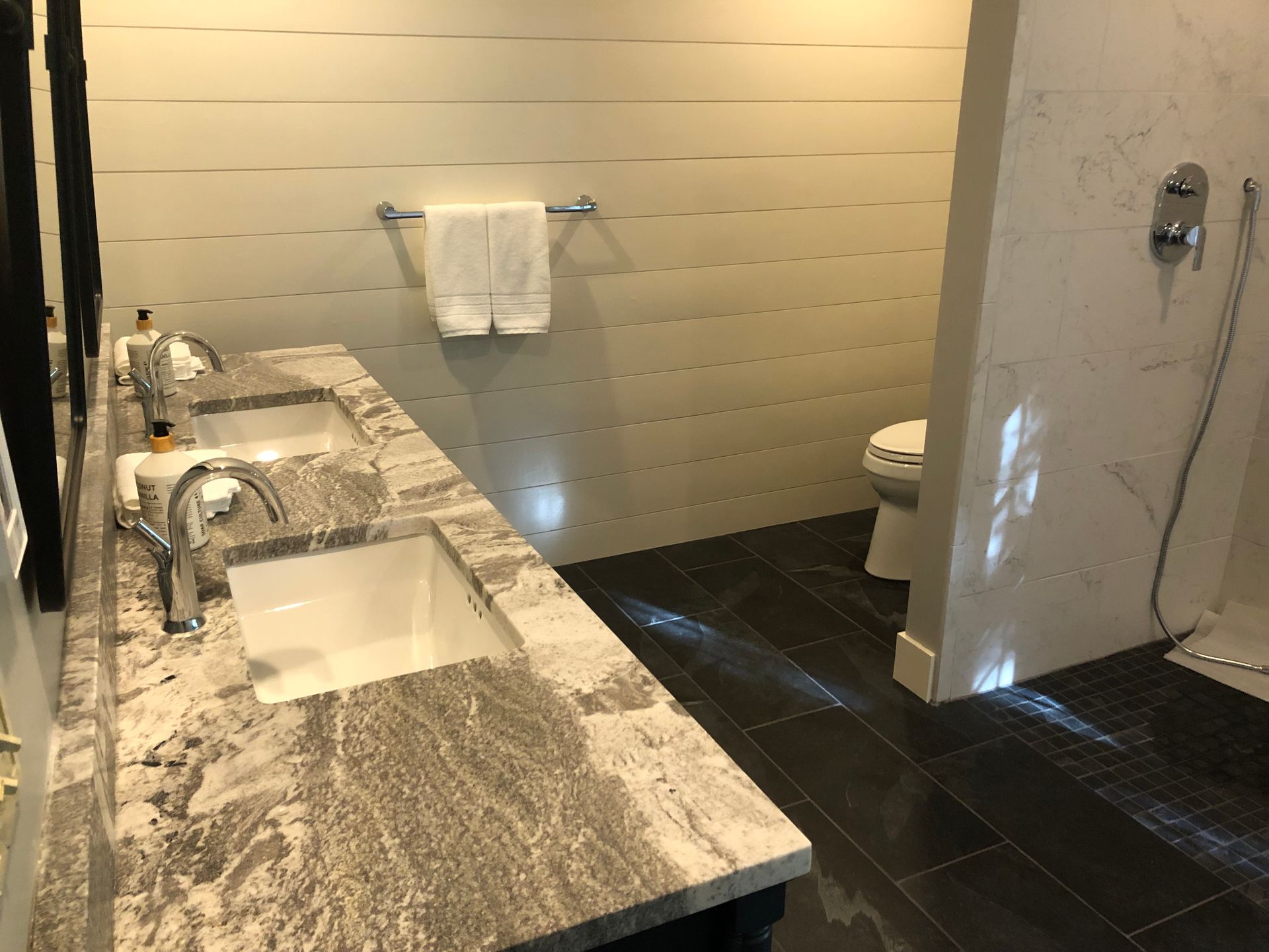 Bathroom with double vanity, white sinks, granite countertop, toilet, and shower.