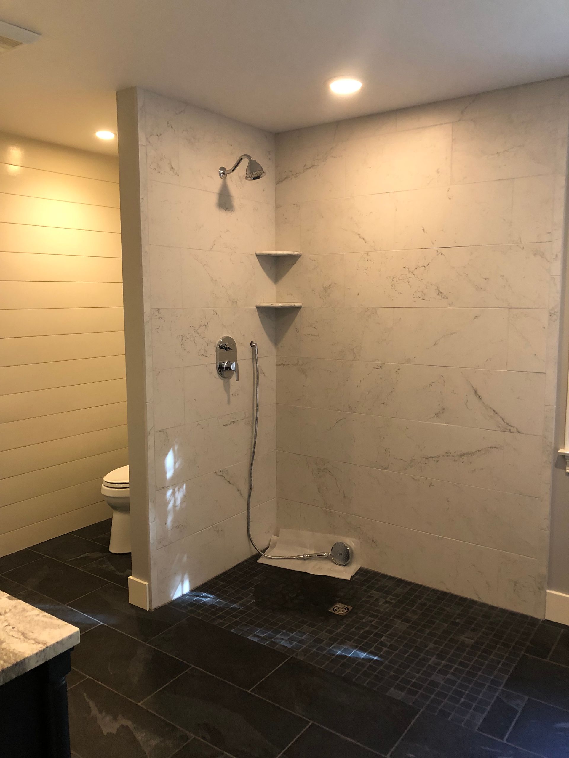 Modern bathroom with marble shower, dark tile floor, and a toilet.