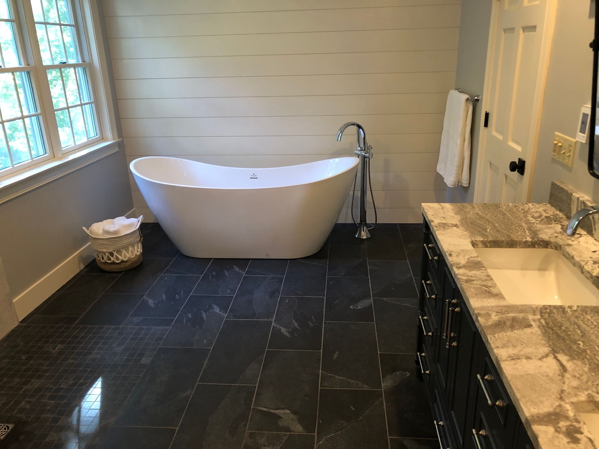 Bathroom with a white freestanding bathtub, dark tile floor, and a vanity.