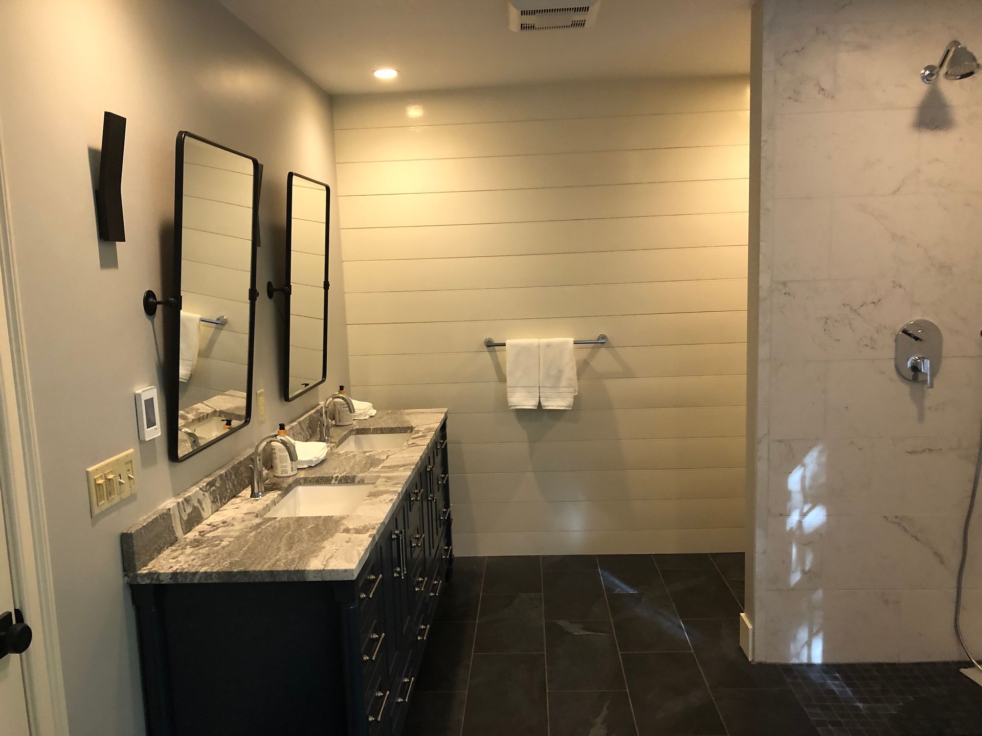 Bathroom with double sinks, two mirrors, and a shower. Navy blue vanity, gray countertops, and white towel bar.