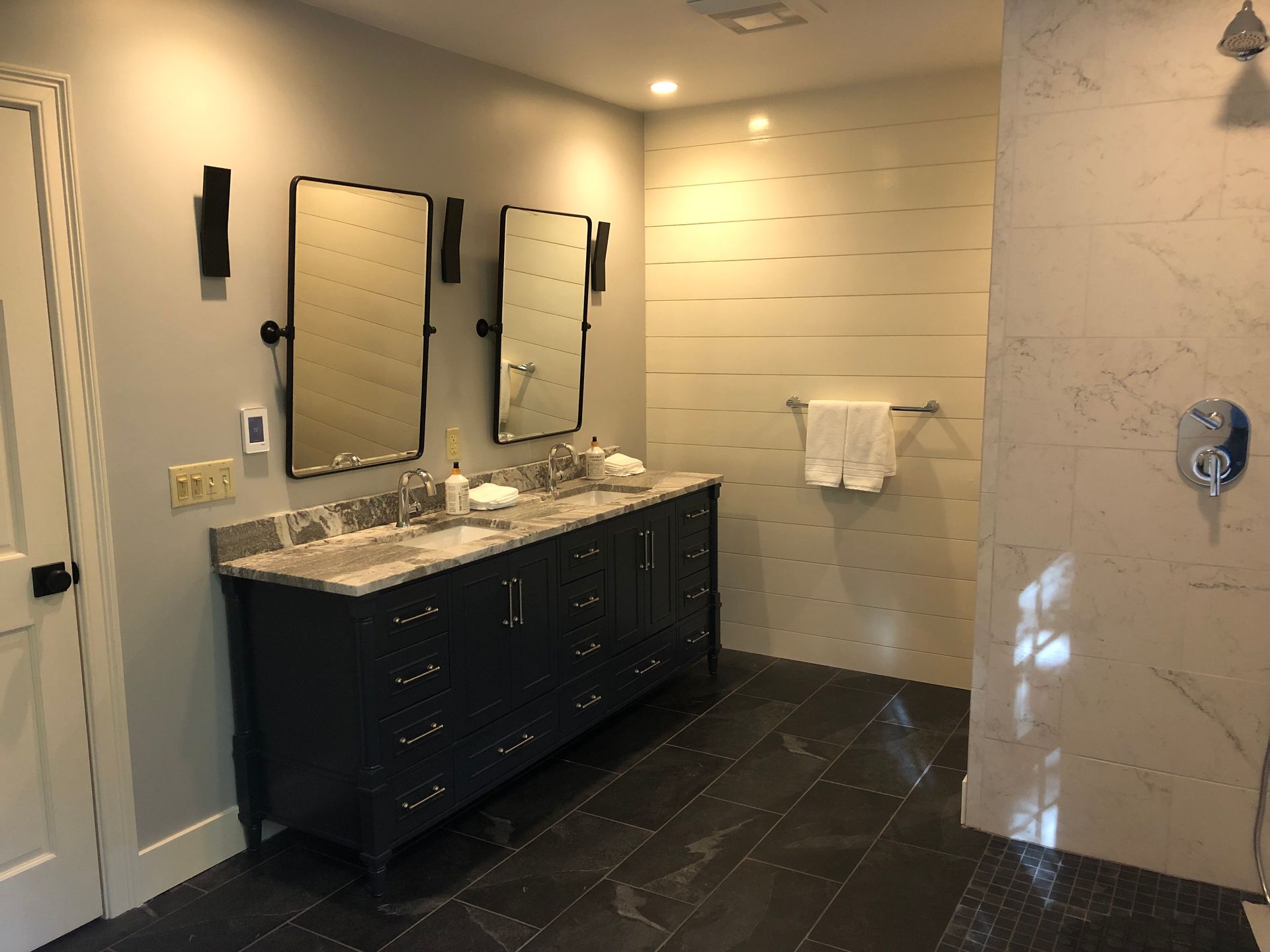 Bathroom with dark blue vanity, two mirrors, and a shower with white textured walls.