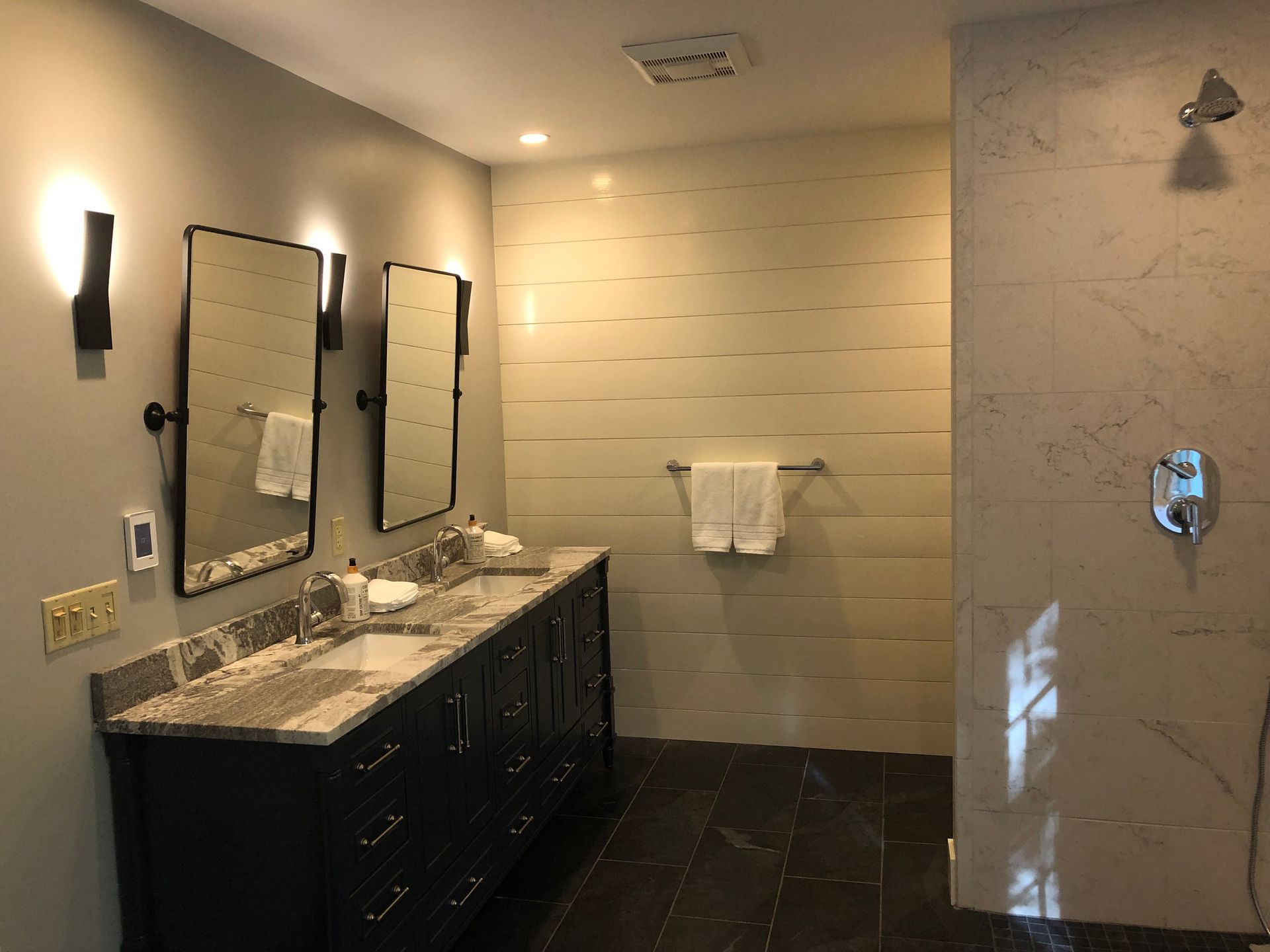 Bathroom with vanity, mirrors, shower, and towel rack. Light gray walls, dark cabinetry, and marble accents.