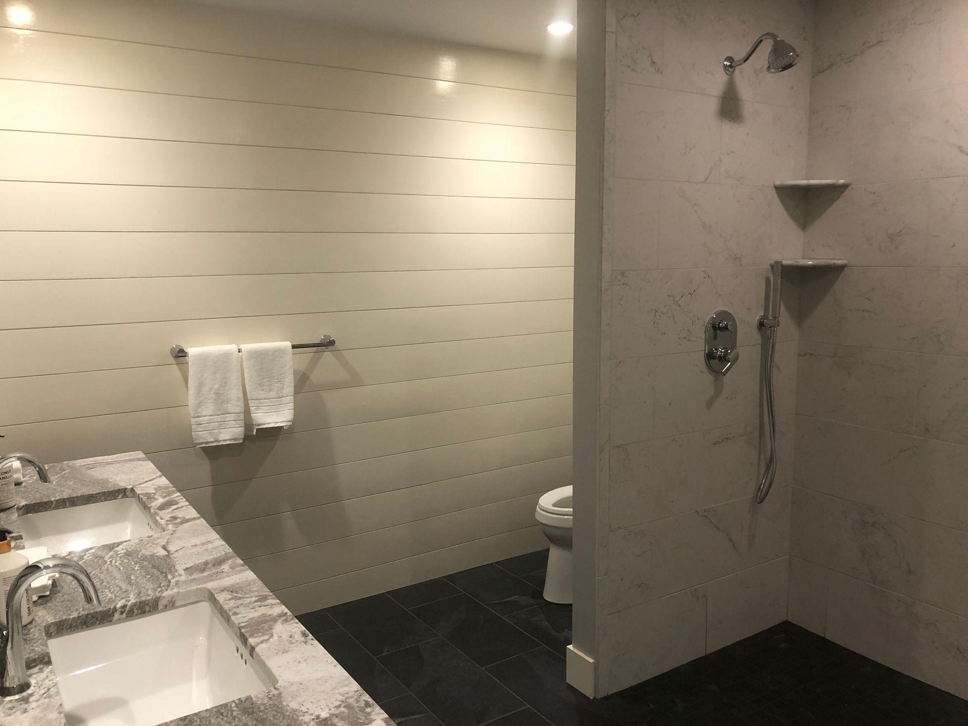 Bathroom with double sink vanity, shower, and toilet. Gray and white color scheme.
