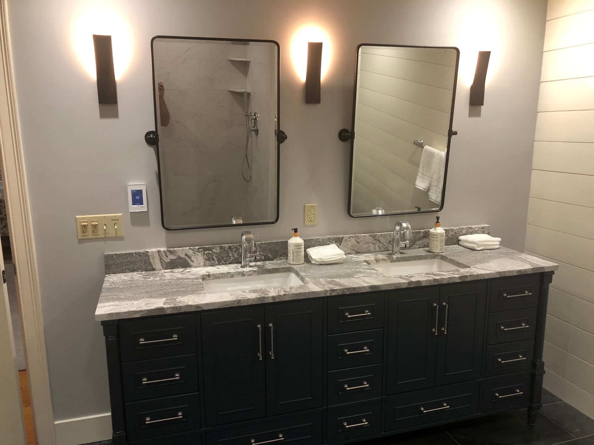 Bathroom with dark blue double vanity, granite countertop, two mirrors, and wall-mounted sconces.