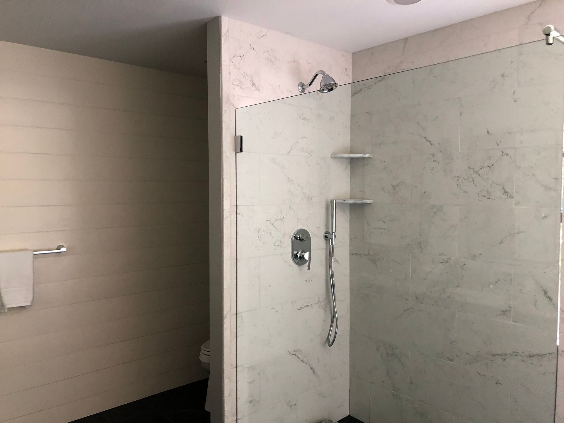 Modern bathroom with glass shower enclosure and marble-like tile walls. White towel and fixtures.