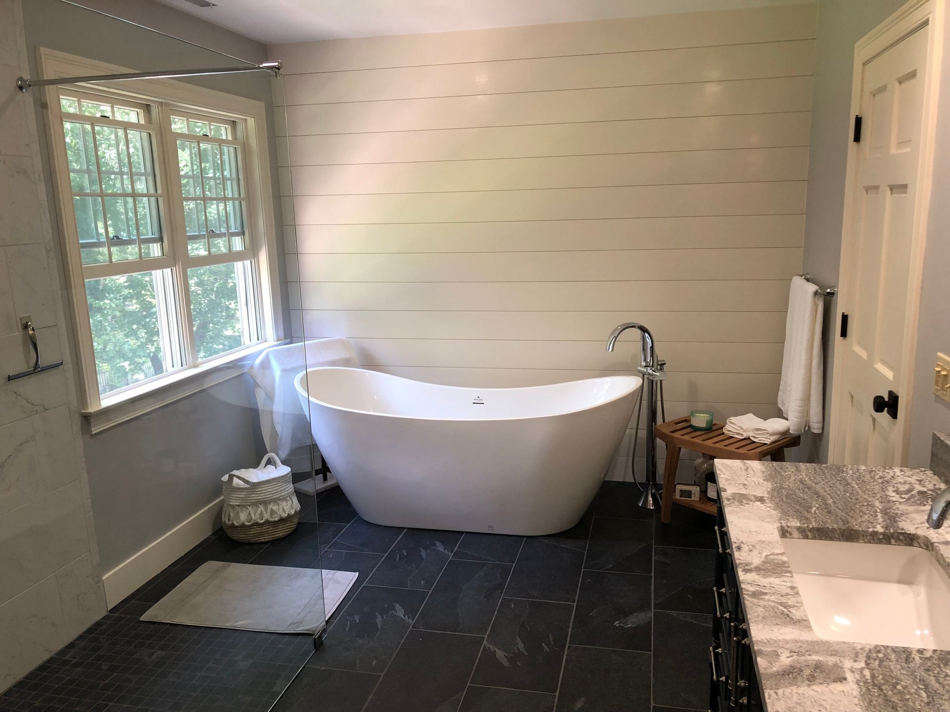 Bathroom with white soaking tub, dark tile floor, and shiplap wall.