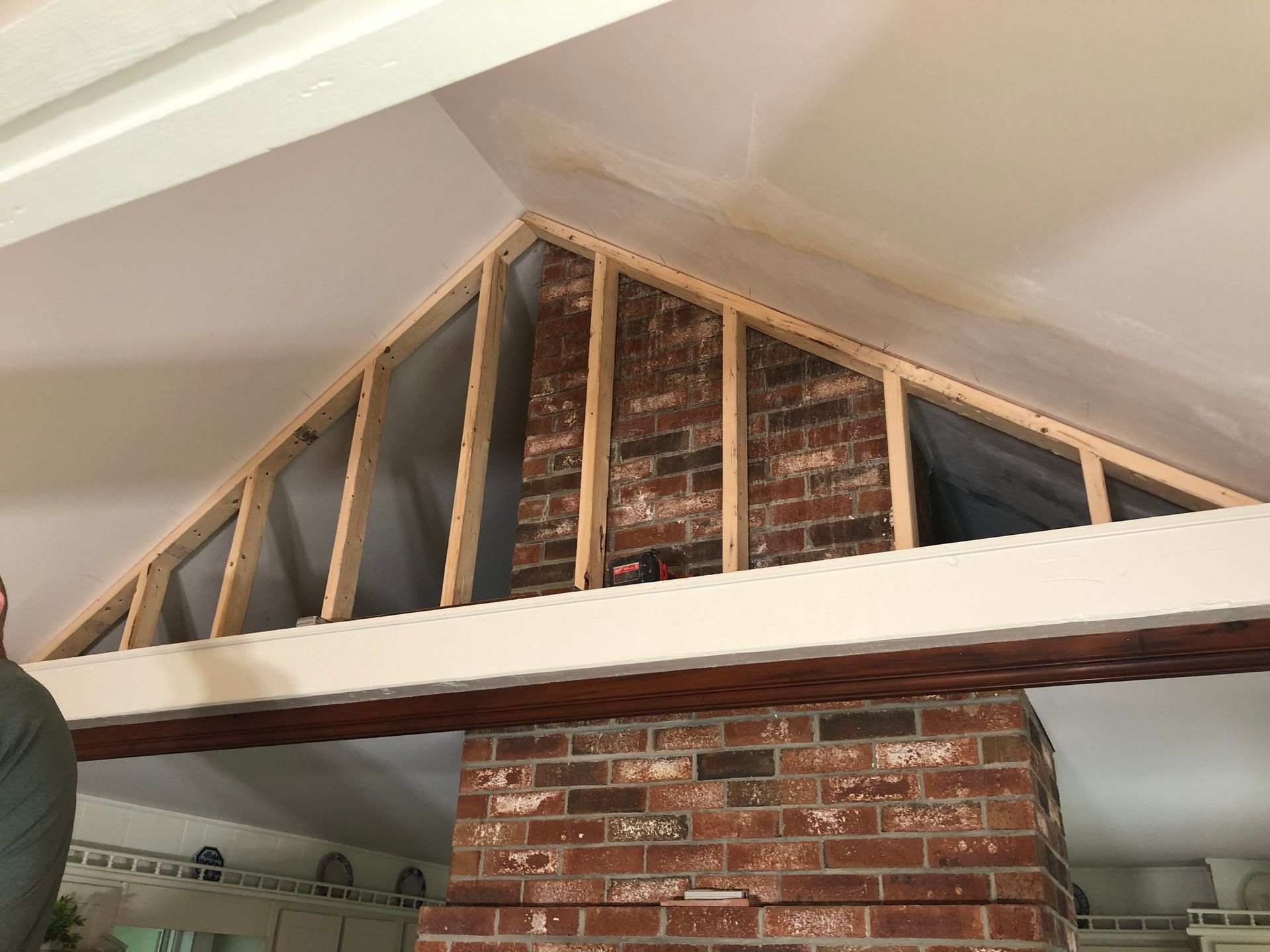 Brick chimney with wooden framing in an attic space. Framing painted white, brick is red.