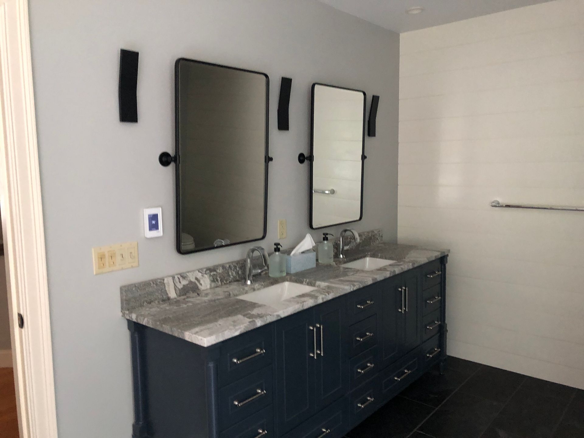 Bathroom with blue vanity, granite countertop, two mirrors, and black sconces.