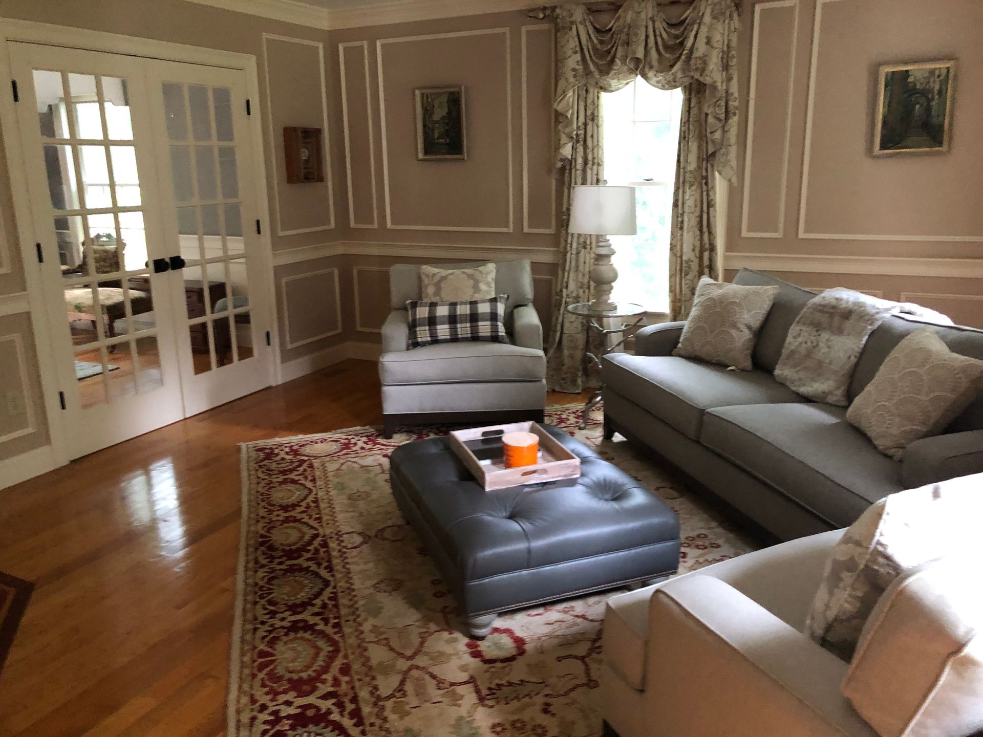 Living room with gray sofa, armchairs, rug, and French doors.